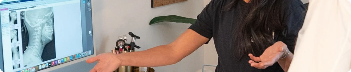 A patient at the front desk of Huntington Beach Chiropractic beside a monitor showing her cervical spine X-ray