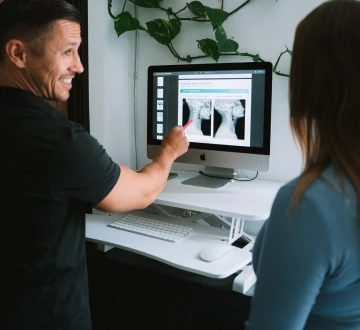 Dr. Michael VanDerschelden pointing at X-ray images on a monitor while a patient looks on