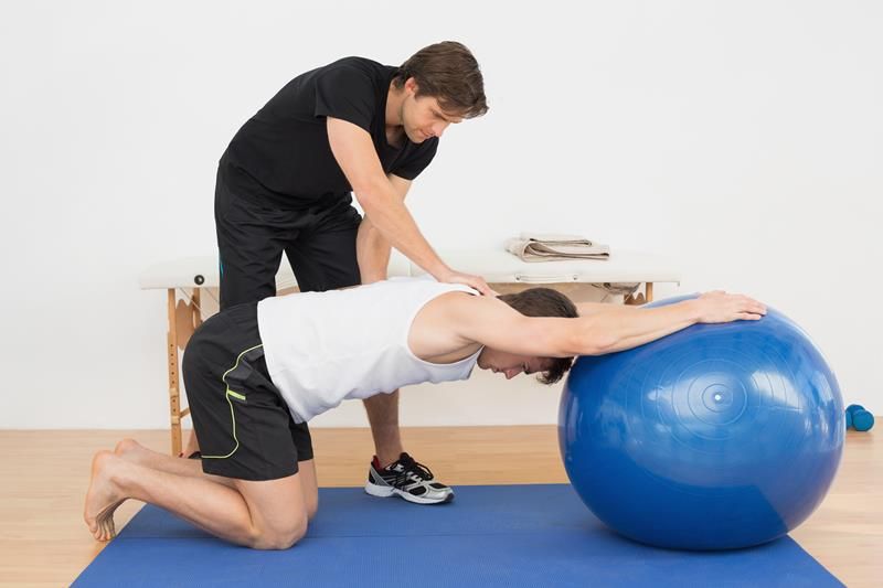 man stretching on medicine ball with chiropractor assisting